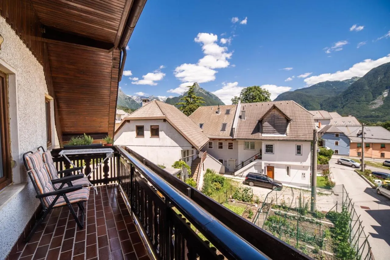 Balkon apartmaja 1 z rjavo leseno ograjo, spodaj vrt in hiše, zadaj zelene gore