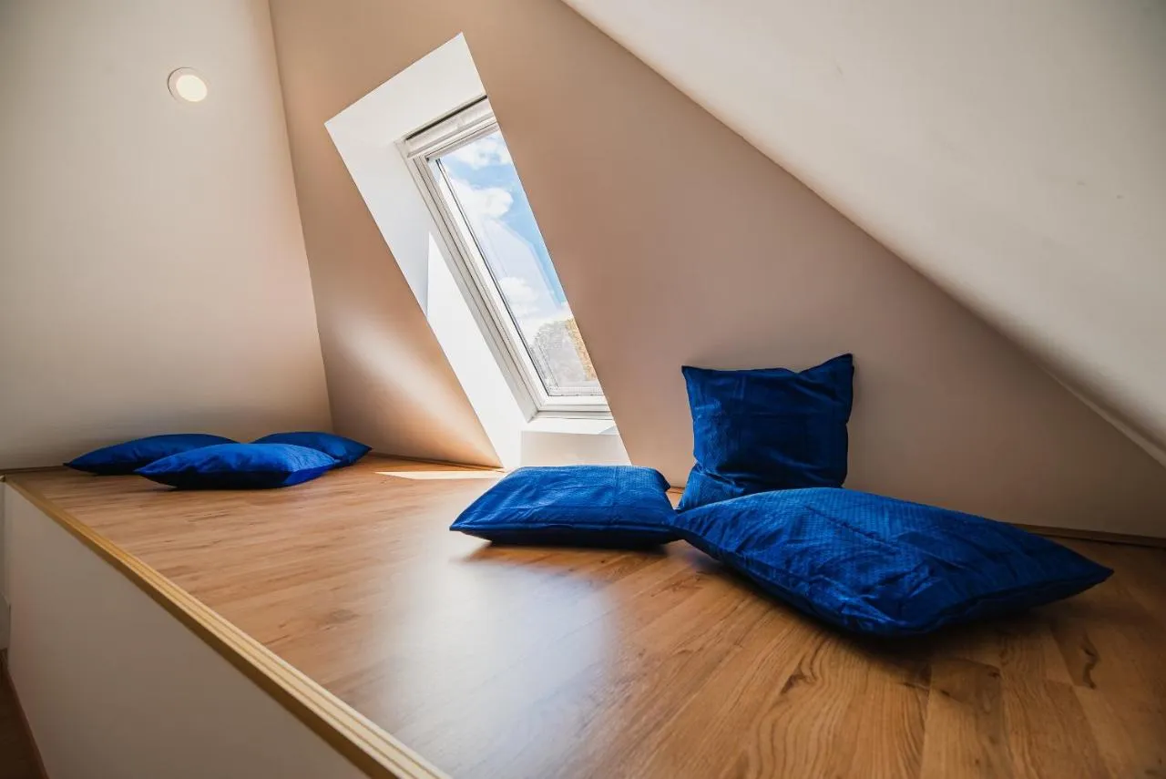 Lesena ploščad z modrimi blazinami pod strešnim oknom v mansardi apartmaja 1
